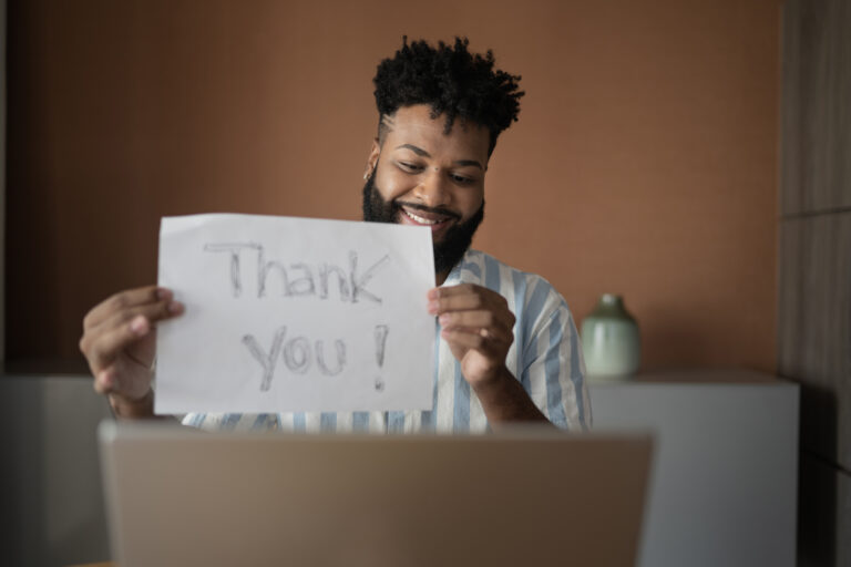 Person holding up a "thank you" sign in front of a laptop.