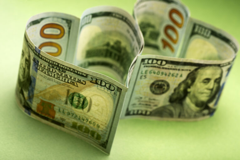 Two heart-shaped hundred dollar bills on a green background: