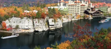 White cliffs and the Mohonk Mountain House reflected in Mohonk Lake, surrounded by colorful Autumn trees in the Shawangunk Mountains of New York