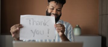 Person holding up a "thank you" sign in front of a laptop.