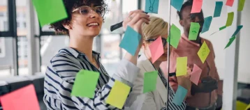 Multiracial team at work writing strategy ideas on sticky notes on the glass wall while having a meeting in the office. Business project planning.