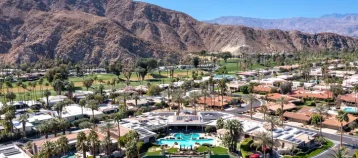 Aerial view of a large home and a residential community in a suburban area with a golf course and mountains in the distance.