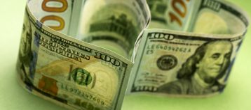 Two heart-shaped hundred dollar bills on a green background: